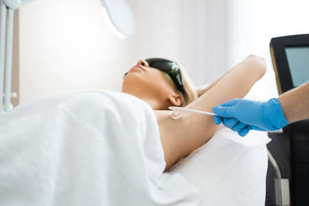 Applying hair removal gel under the arms. Woman at a laser epilation session with a modern laser in a beauty studioの写真素材