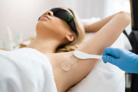 Applying gel for laser epilation to female client armpit area. Woman lying during laser hair removal procedureの写真素材
