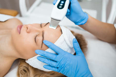 Close up of relaxed woman receives ultrasonic facial cleansing from the hands of a professional cosmetologis. Face skin peeling in a beauty salonの写真素材