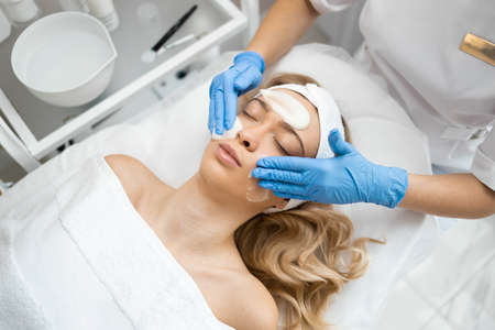 Dermatology doctor in gloves is applying facial cleansing foam on woman's face, massage skin in cosmetology clinic.の写真素材