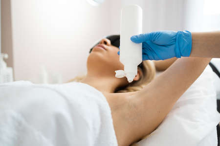 Cosmetologist applies laser hair removal gel to female client's armpit. Laser hair removal processの写真素材