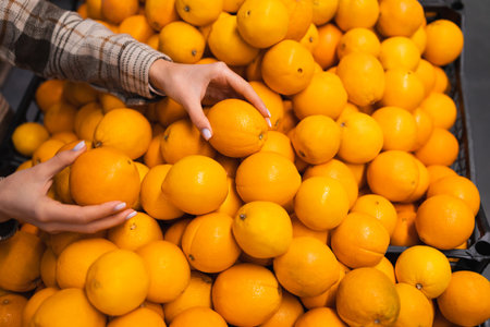 Close up of woman's hands taking oranges from supermarket counter. Shopper chooses oranges at the...