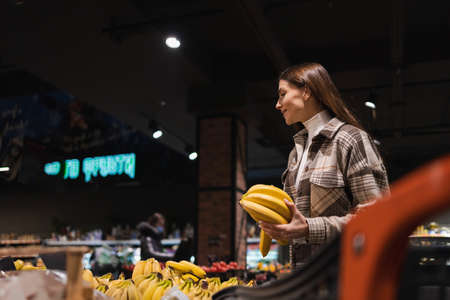 Girl buys bananas in the fruit section of the supermarketの写真素材