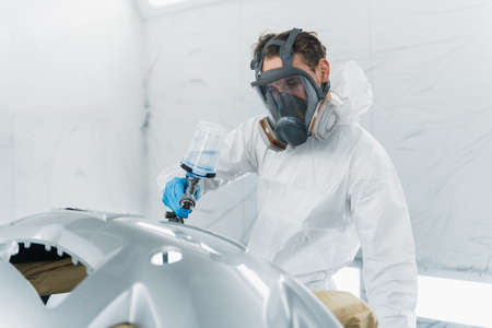 Auto painter varnishing a car body part in a painting booth. Repairman restores vehicle body partsの写真素材
