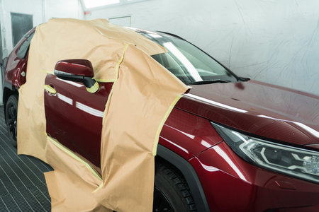 Car covered with masking tape and paper is in the booth for painting before repaint or polishing