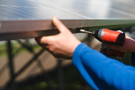 Close-up of the hand of engineer who tightens the bolts of the solar panels to the metal base with a electric drillの写真素材