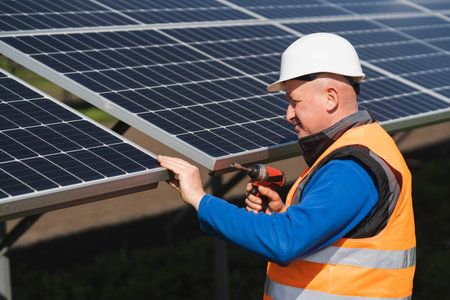 Solar power plant worker with electric wrench in his hands inspects panels