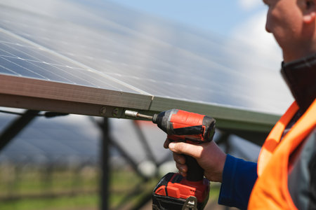 Close-up view of engineer who tightens the bolts of solar panels to a metal base with electric drillの写真素材
