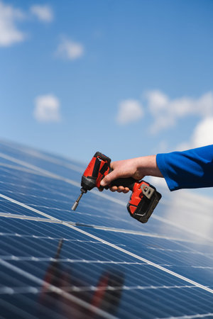 Close up view of engineer working with electric screwdriver drill installing solar panel to metal...