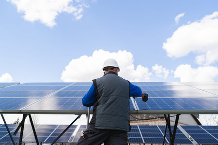 Back view of a man works with a drill screwdriver on solar panels