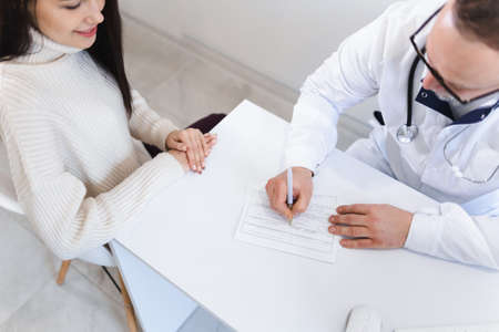 Top view of patient and doctor taking notes. The physician fills out the patient's disease cardの写真素材