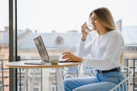 Pretty girl drinks water while working at laptop in cafeの写真素材