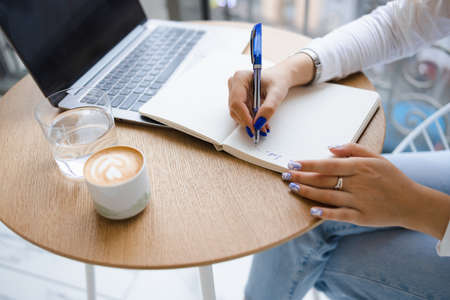 Close-up view of a woman's hands writing notes in a notebook. Girl working in a cafeの写真素材