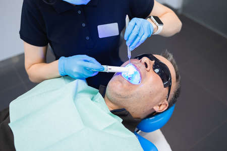 Female doctor dentist uses ultraviolet lamp while filling the male patient's teethの写真素材