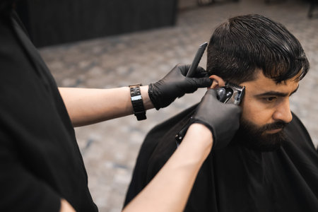 Hands of a barber in black gloves cutting a man with a clipper. Hairdresser doing a haircut to a...