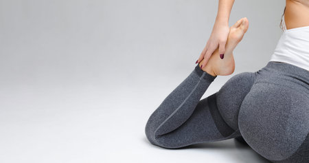 Woman doing yoga and stretching barefoot in studio on gray background