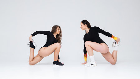 Two athletic girls in black bodysuit are warming up in the studio on a white backgroundの写真素材