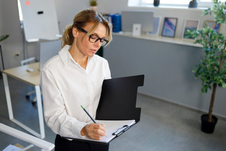 Serious business woman writing on clipboard in office