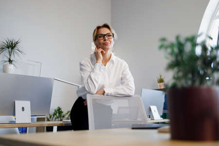 Joyful mature business woman leaning against the back of the chair in the office. Portrait of elegant female secretaryの写真素材