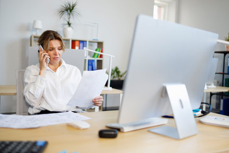 Woman accountant indignantly looks at documents and talks on the smartphone