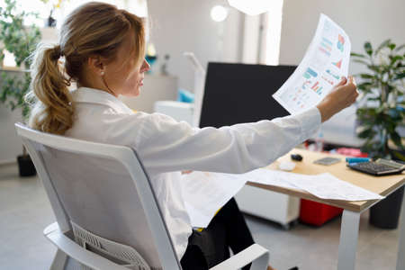 Female accountant examines documents with financial diagram and charts while sitting in a chair at the workplaceの写真素材