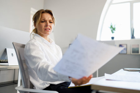 Dissatisfied business woman examines documents at her workplace in office