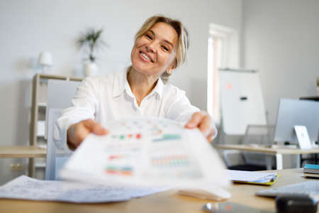 Happy middle aged businesswoman giving papers in officeの写真素材