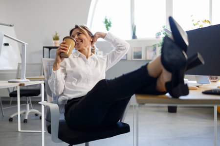 Happy business woman drinking coffee putting legs on the table