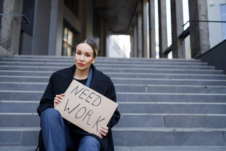 Sad woman sits on the stairs near a office building with a sign board need job