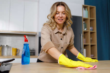 Woman in yellow rubber gloves cleaning wooden kitchen countertopの写真素材