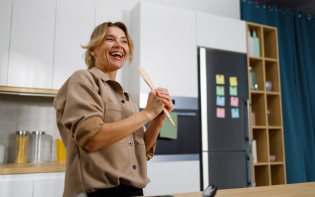 Portrait of smiling mature woman singing in kitchen with wooden spatula
