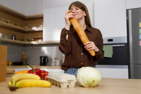 Woman with a baguette in her hands and many products on the kitchen countertop
