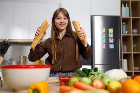 Woman with a broken baguette in her hands at the kitchenの写真素材