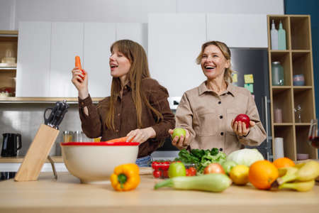 Mature woman and her daughter have fun while cooking in the kitchenの写真素材
