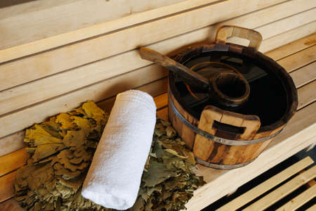 Wooden bucket with ladle, towel and broom on bench in saunaの写真素材