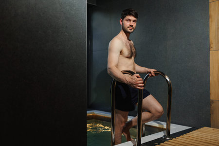 Muscular man descends into the pool in the spa complex