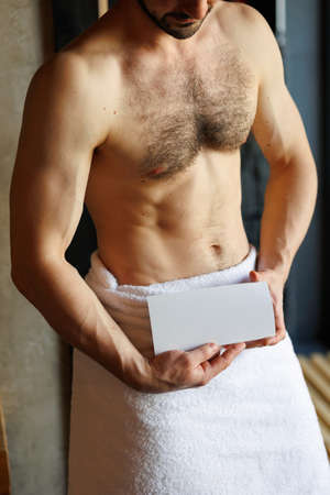 Muscular man in a towel holding a blank flyer in his hands. Spa salon or massage advertising conceptの写真素材