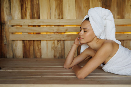 Young woman in white towel lying in wooden saunaの写真素材