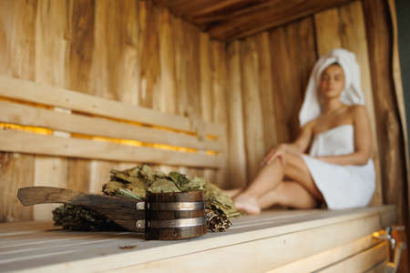 Selective focus on ladle, sauna broom and relaxed woman in towels on backgroundの写真素材