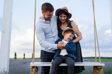 Young family is playing with their son who is sitting on a swing in a lavender field.