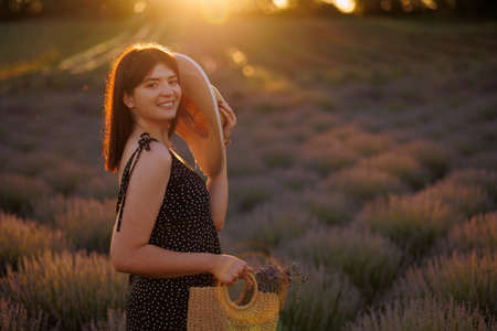 Beautiful girl in a lavender field with a straw hat and a wicker bag in her handsの写真素材