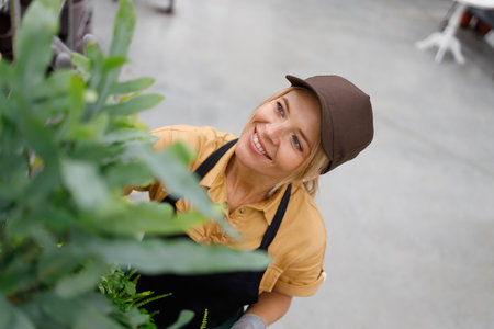 Woman in uniform caring for a green plant in a garden centerの写真素材