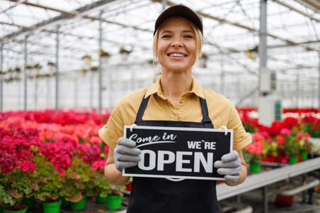 Female florist with sign we are open in greenhouseの写真素材