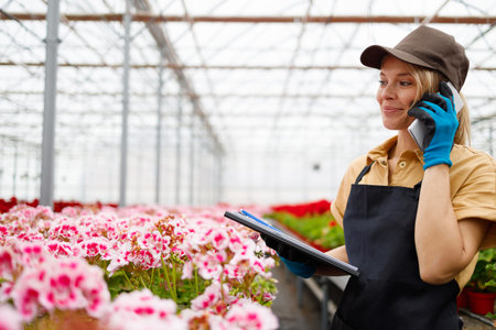 Pretty woman seller of a greenhouse with flowers talking on the phone with a client