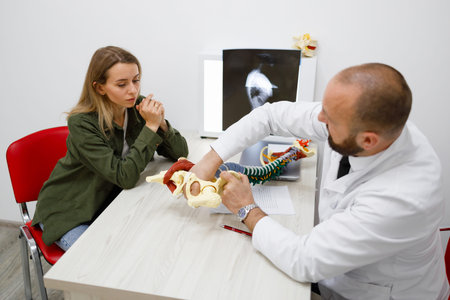 Adult male doctor showing spine model to young female patient