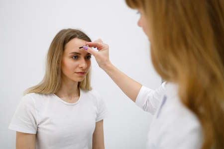 Neurologist doctor makes skin reflex test with special brush on a woman's face skin during medical appointment in clinicの写真素材