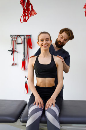 Physiotherapist doctor carefully examines the neck and shoulders of his female patient for defects. Young woman on examination in a rehabilitation clinicの写真素材