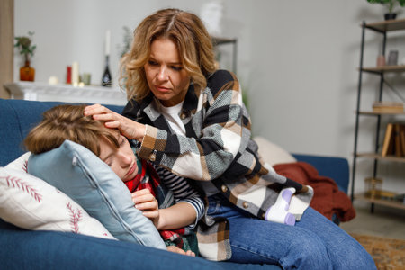 Mother caresses her daughter, who is sleeping on a sofa in the living room, who is ill with fluの写真素材