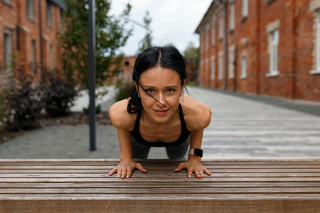 Confident sports woman doing push-ups from the bench outdoors. Female athlete exercising on the city streetの写真素材