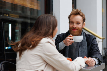 Happy couple drinking coffee and laughing talking to each other sitting at the table of outdoor cafe on city streetsの写真素材
